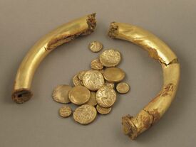 Cet ensemble, comprenant un brassard et des monnaies, constitue un petit dépôt datant des environs de la conquête romaine.